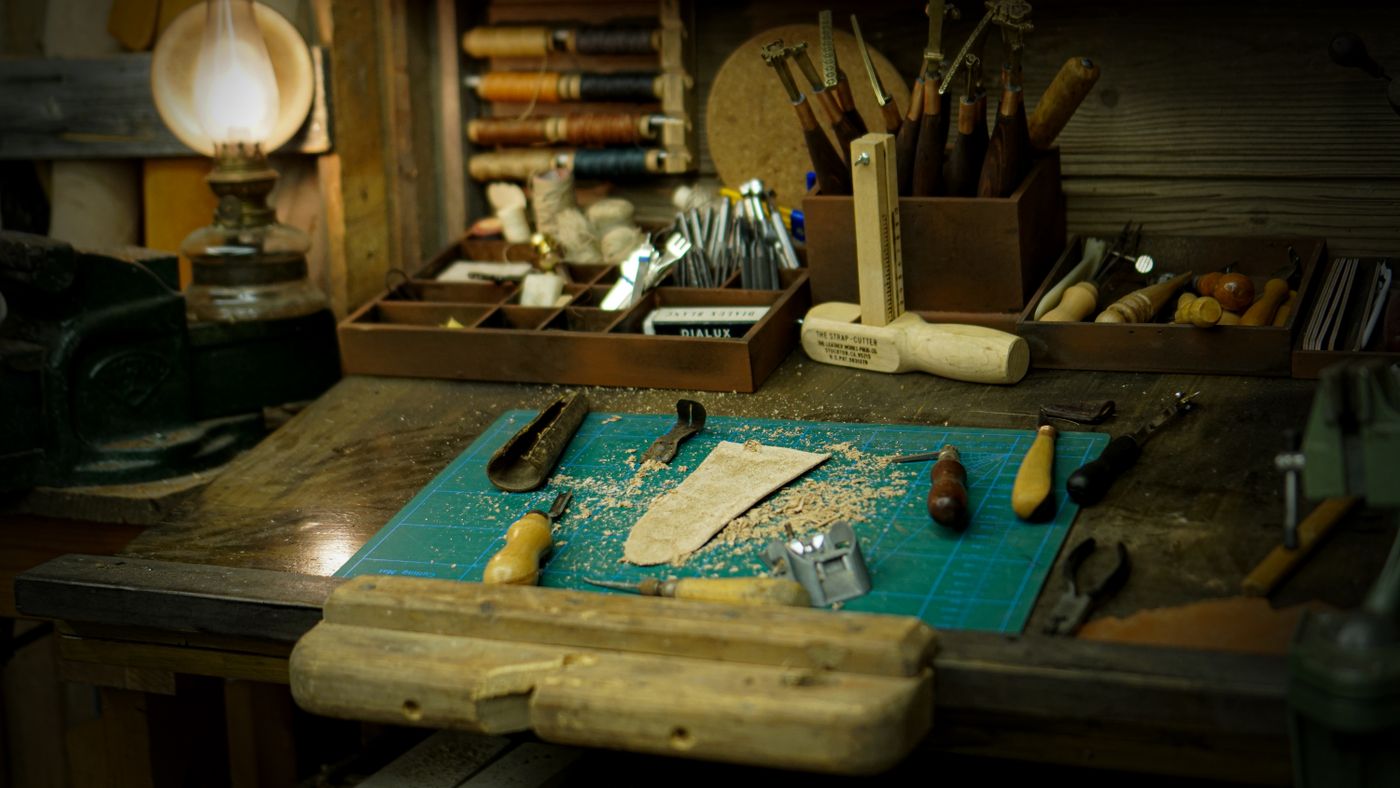 Établi de maroquinerie éclairé par une lampe à huile, outils rangés