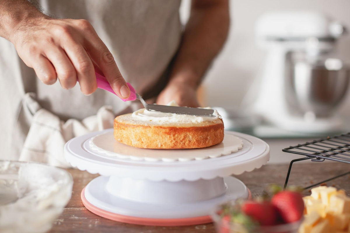 Lissage de la crème à la spatule coudée sur un layer cake posé sur le plateau tournant