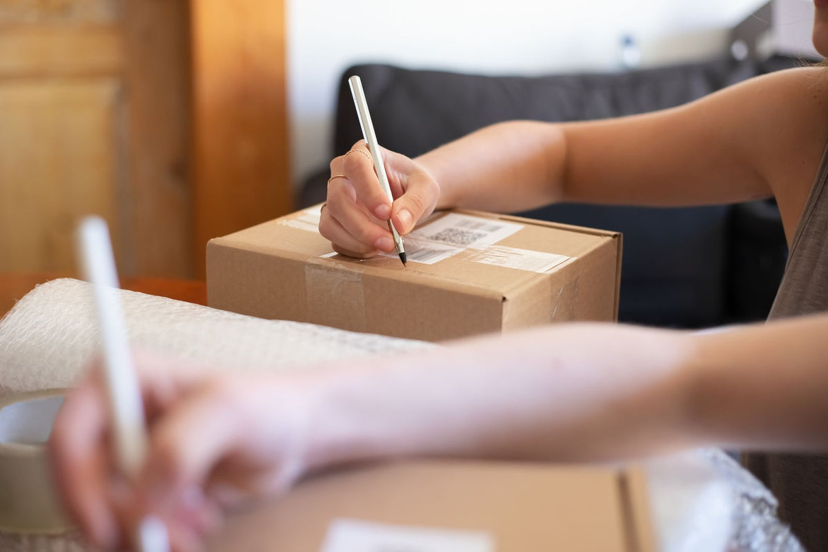 Vendeuse préparant et étiquetant un colis de boutique en ligne