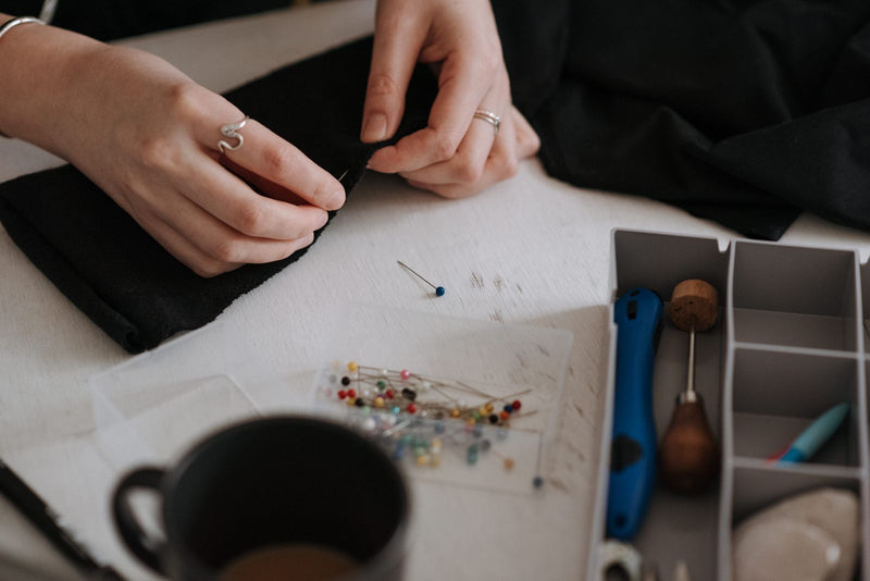 Mains épinglant un tissu noir sur la table de couture