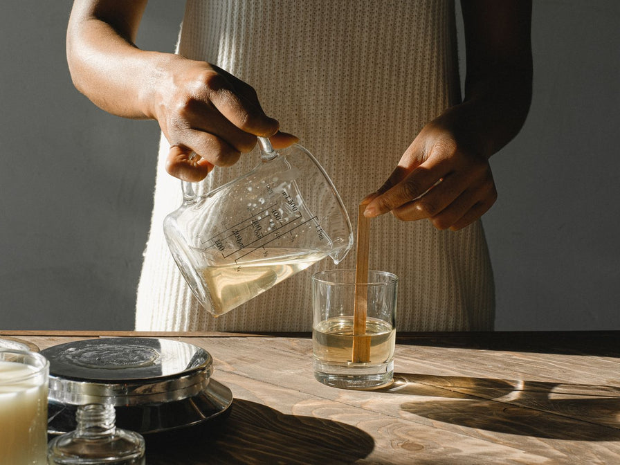 Mains versant la cire fondue dans un contenant de bougie