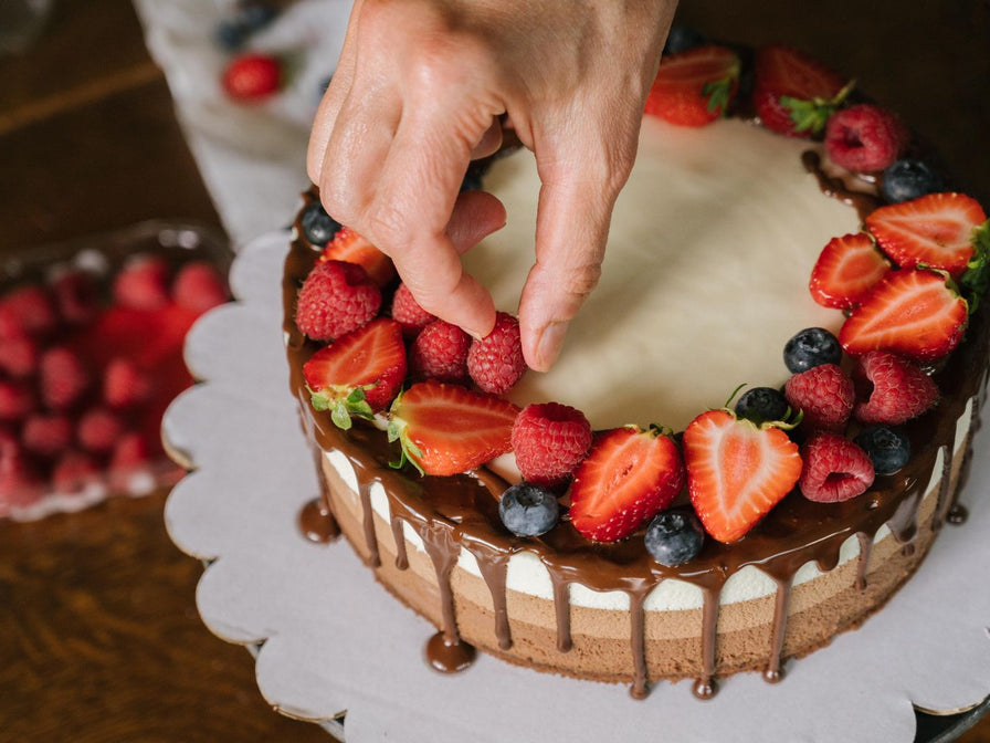 Main déposant des fruits rouges sur un layer cake