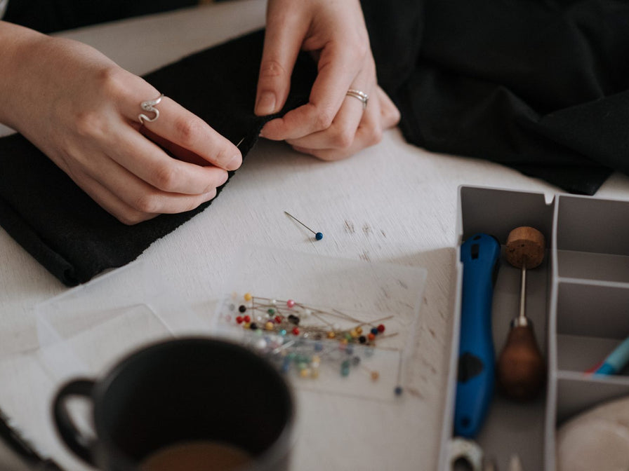 Mains épinglant un tissu noir sur la table de couture