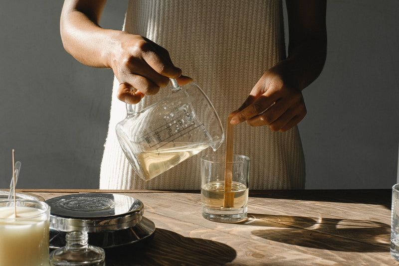 Mains versant la cire fondue dans un contenant de bougie