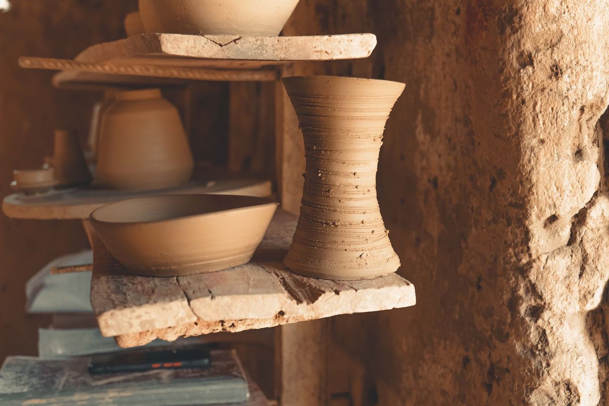 Poteries fraîchement tournées séchant en rangées sur des étagères en bois dans la lumière dorée de l'atelier