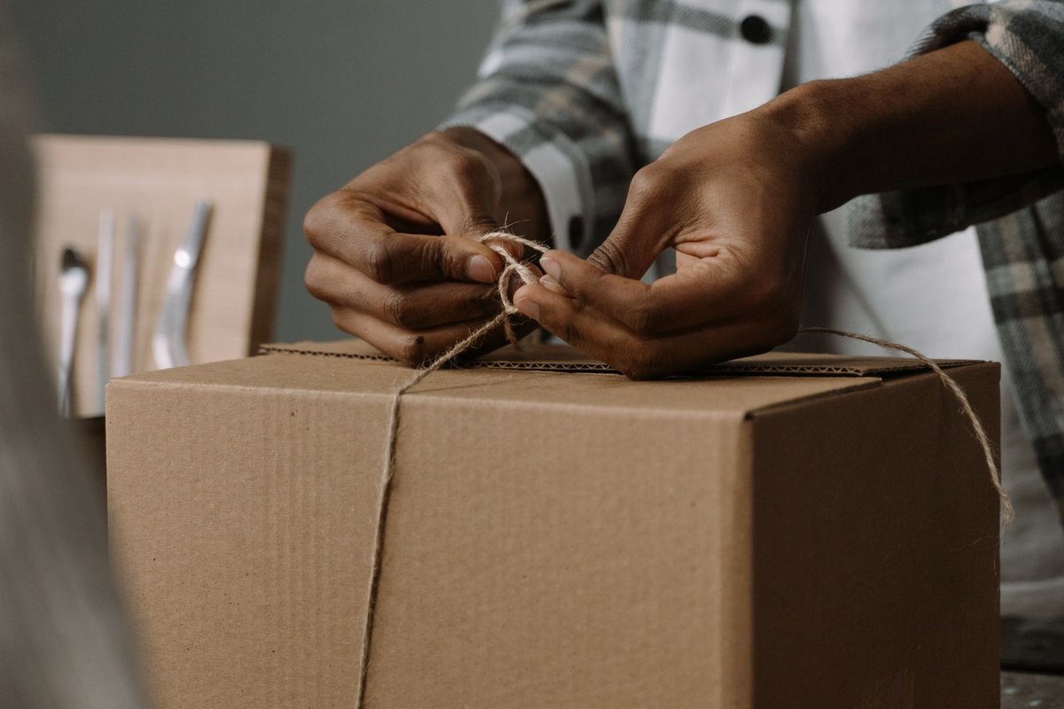 Mains nouant une ficelle autour d'un colis en carton avant l'expédition