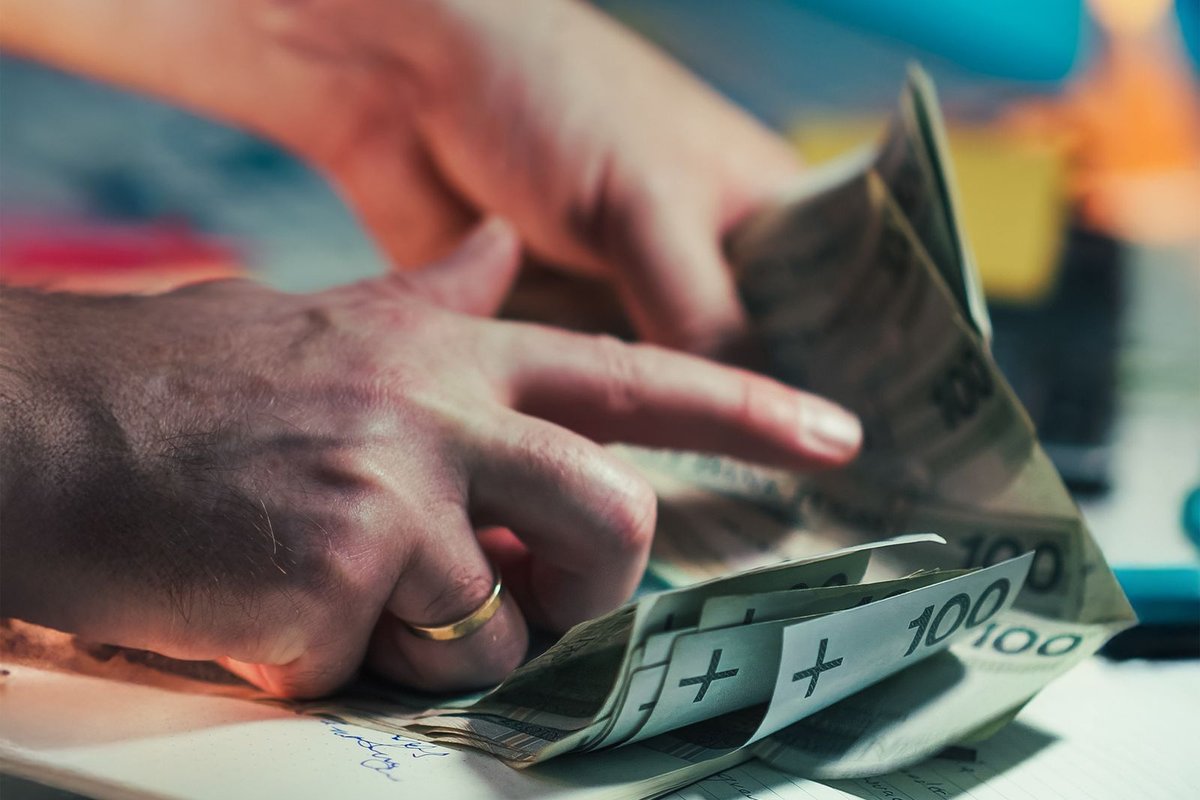 Mains comptant les billets de la recette au-dessus d'un carnet, lumières du marché floues en arrière-plan
