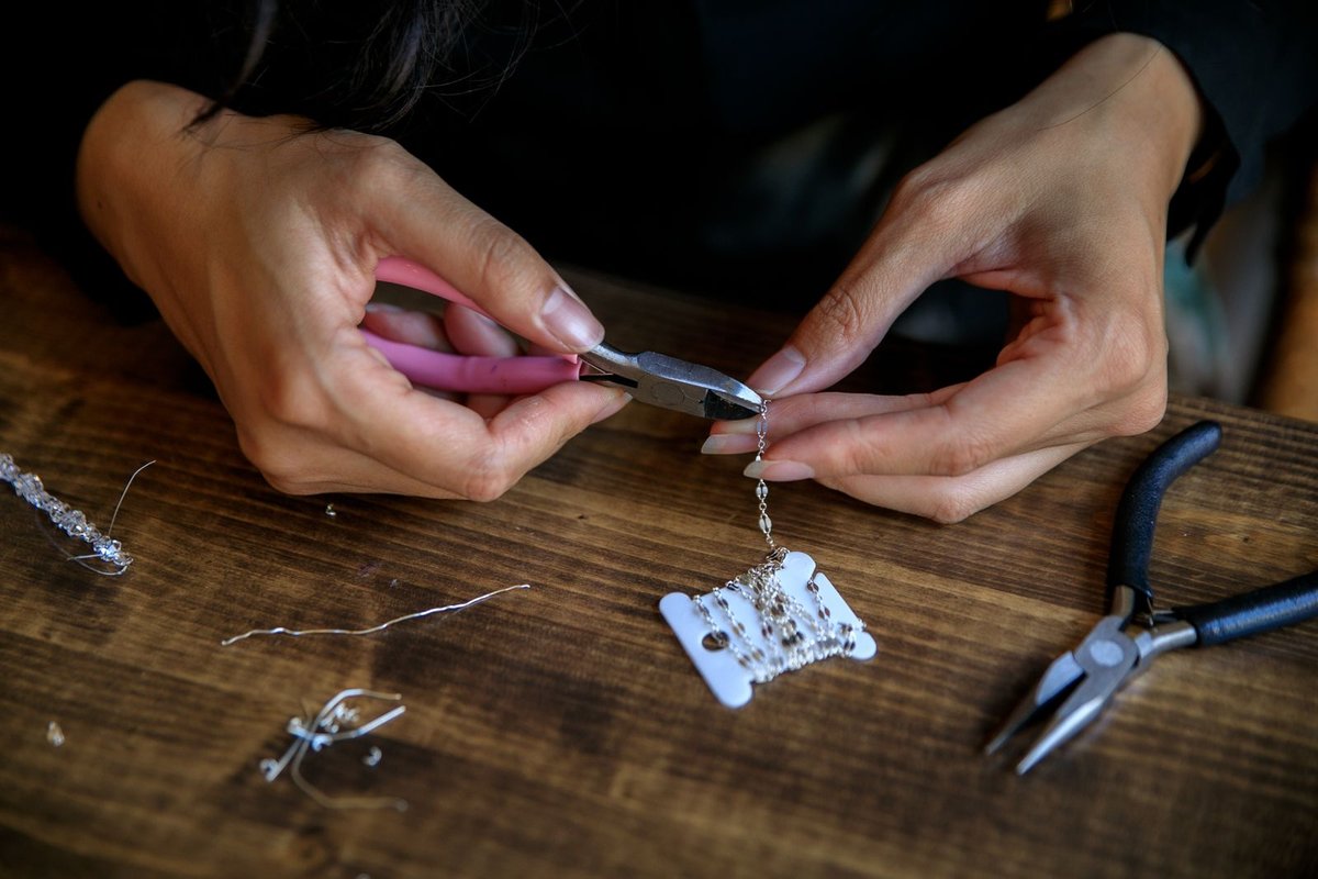 Ouverture d'un maillon de chaîne à la pince pour un bijou fait main, fil et breloques sur l'établi