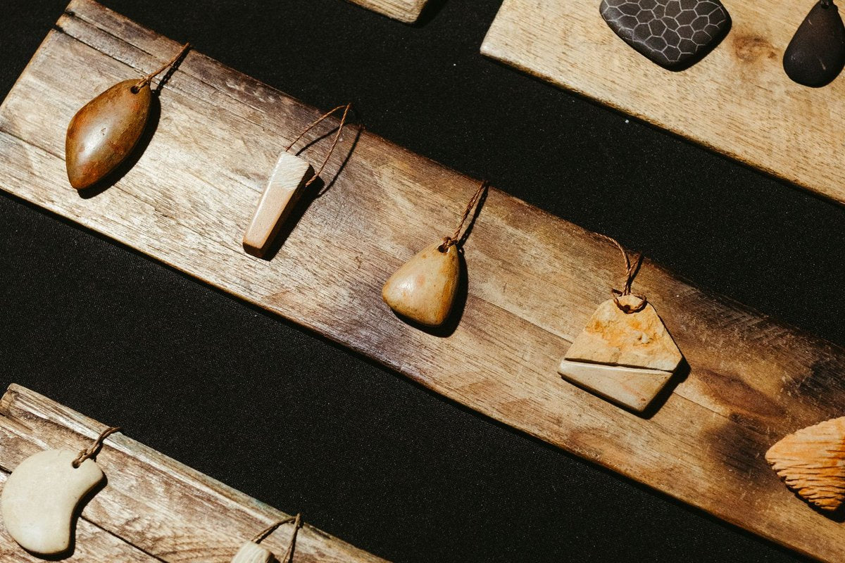 Pendentifs en pierre polie alignés sur des planches de bois flotté, présentoir d'un stand de créateur