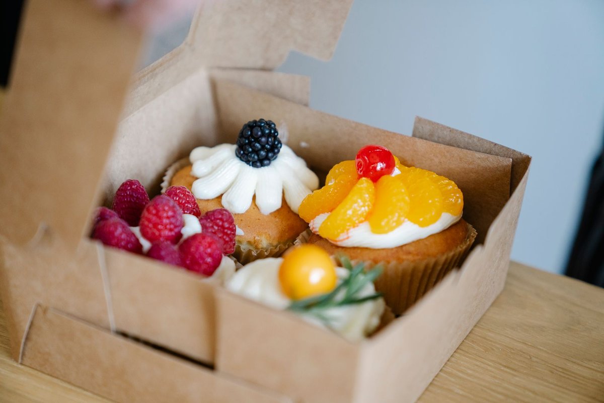 Boîte de transport en kraft ouverte sur quatre gâteaux individuels décorés de fruits frais