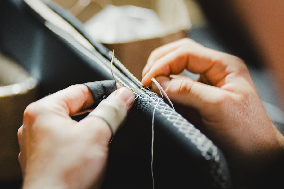 Couture sellier à deux aiguilles sur une pièce de cuir noir maintenue à la main