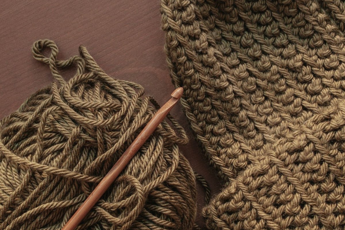Bonnet au crochet terminé posé à côté de sa pelote de laine kaki et de son crochet en bambou