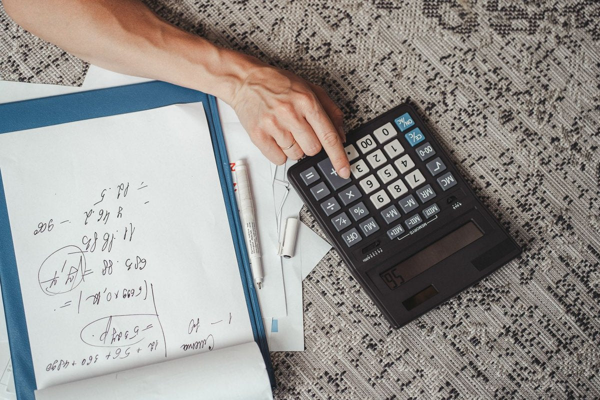 Main pianotant sur une calculatrice à côté d'un bloc-notes couvert de calculs manuscrits