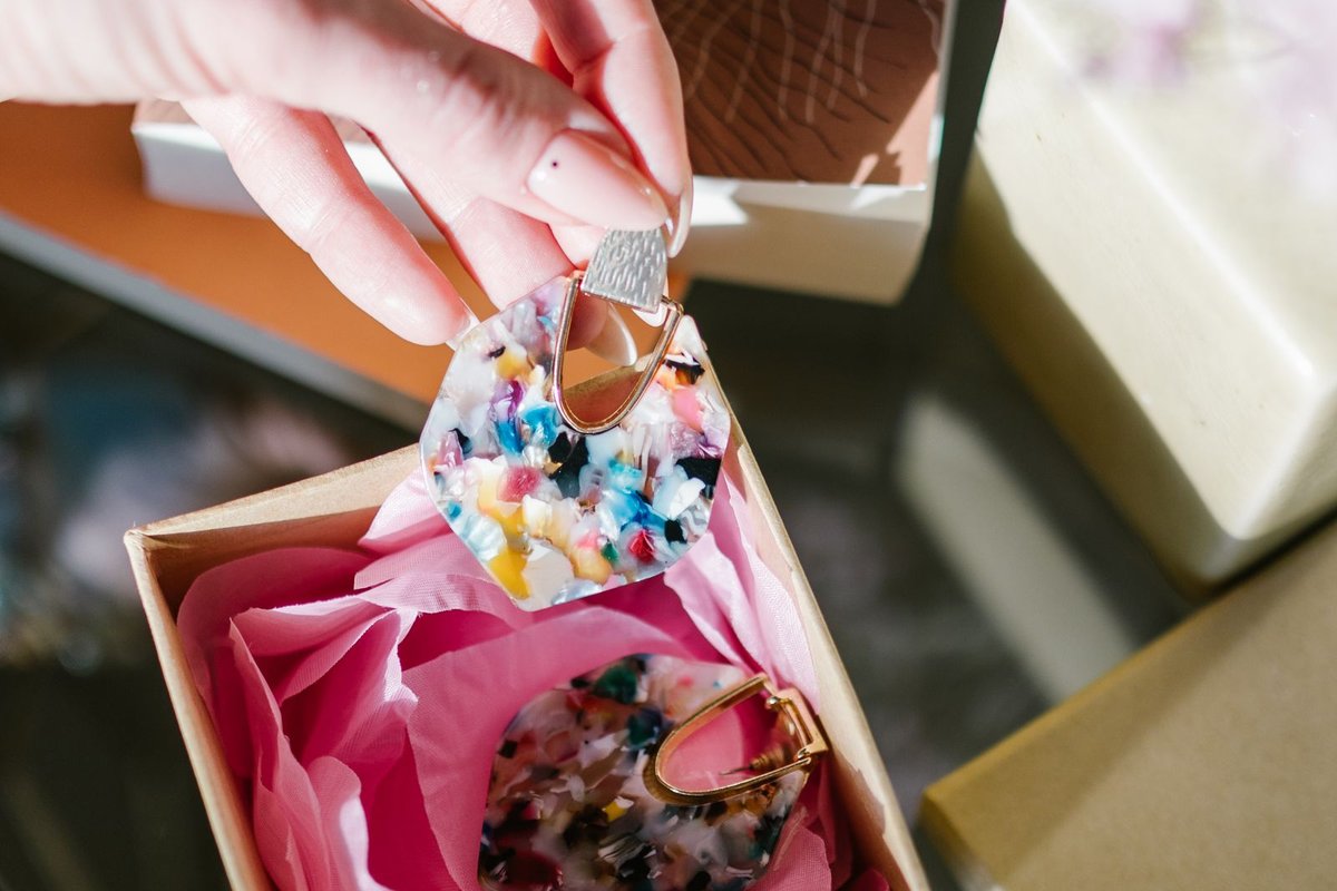 Main déposant la seconde boucle d'oreille dans une boîte cadeau garnie de papier de soie rose