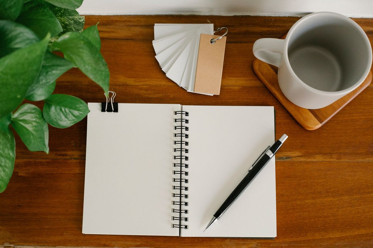 Carnet ouvert, stylo, étiquettes kraft et tasse posés sur une table en bois d'atelier